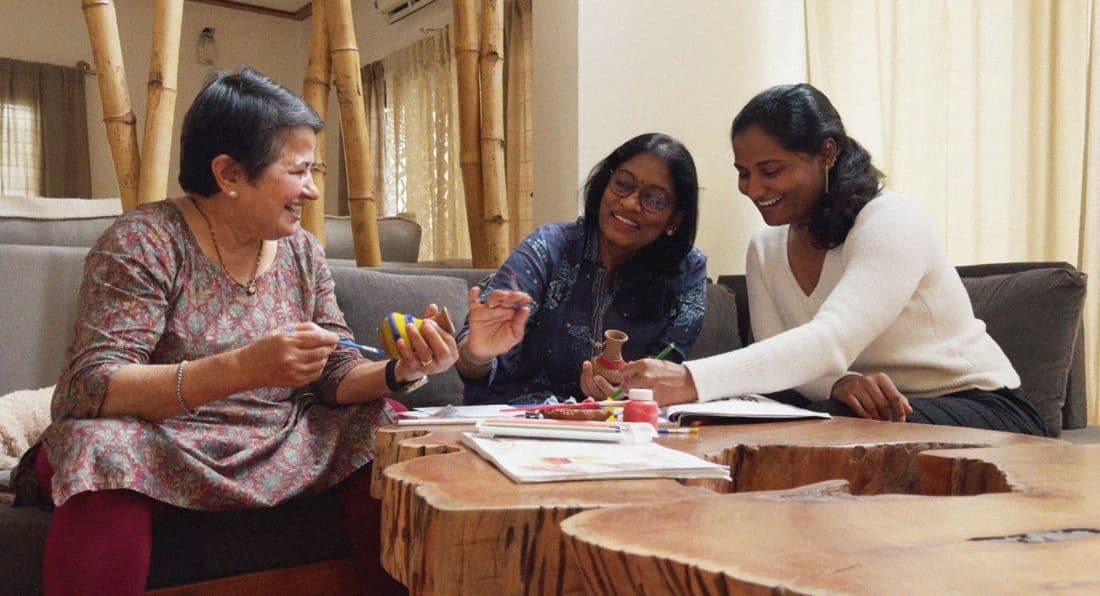 Three women painting clay pots at home, laughing